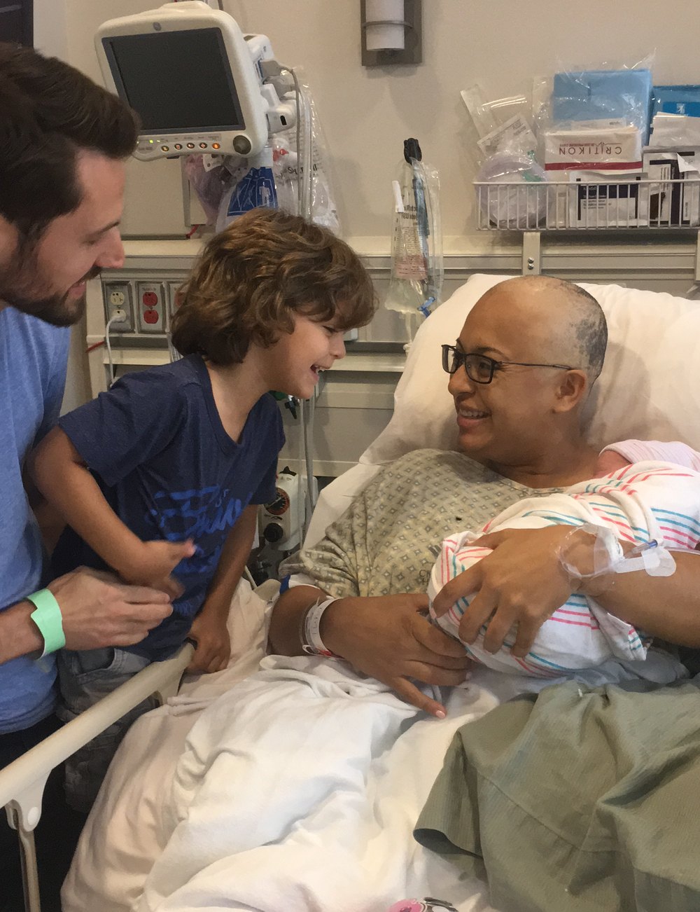 Susana in a hospital bed holding her newborn, with her husband and older son beside her